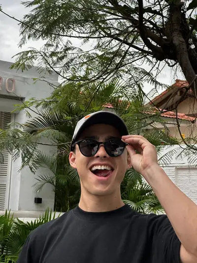 Sonriendo con gorra negra y lentes, polera negra UEBOS