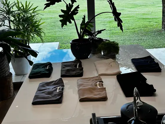 Poleras UEBOS dobladas sobre una mesa, con el jardín detrás del ventanal